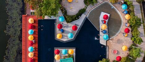 An aerial view of a swimming pool area with multiple colorful umbrellas, seating areas, and surrounding greenery.