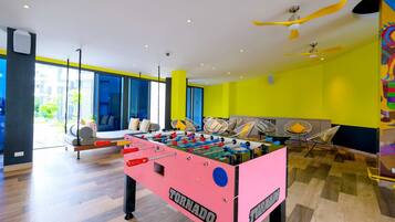 Un espace intérieur lumineux, agrémenté d’un baby-foot, d’un coin salon avec des chaises et d’une grande fenêtre offrant une vue sur l’extérieur.