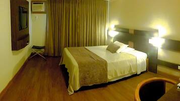 Una habitación de hotel con cama, escritorio, silla, televisor y cortina.