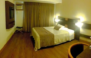 Una habitación de hotel con cama, escritorio, silla, televisor y cortina.