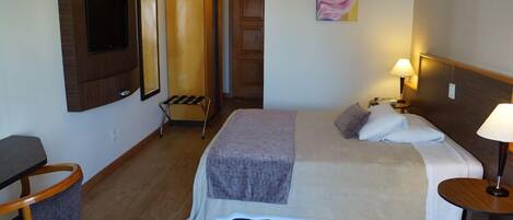 A hotel room with a bed, bedside table, lamp, chair, and a TV mounted on the wall.