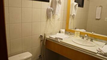 A bathroom with a toilet, sink, and mirror. There is a hairdryer and a phone on the wall.