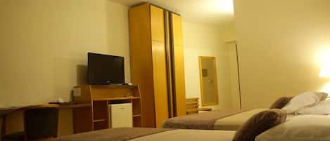 A hotel room with two beds, a television, a wardrobe, and a desk with a chair.
