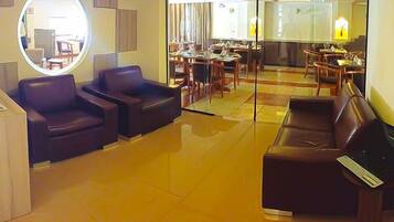 A hotel lobby with leather seating, a round mirror, and a dining area visible through glass partitions.