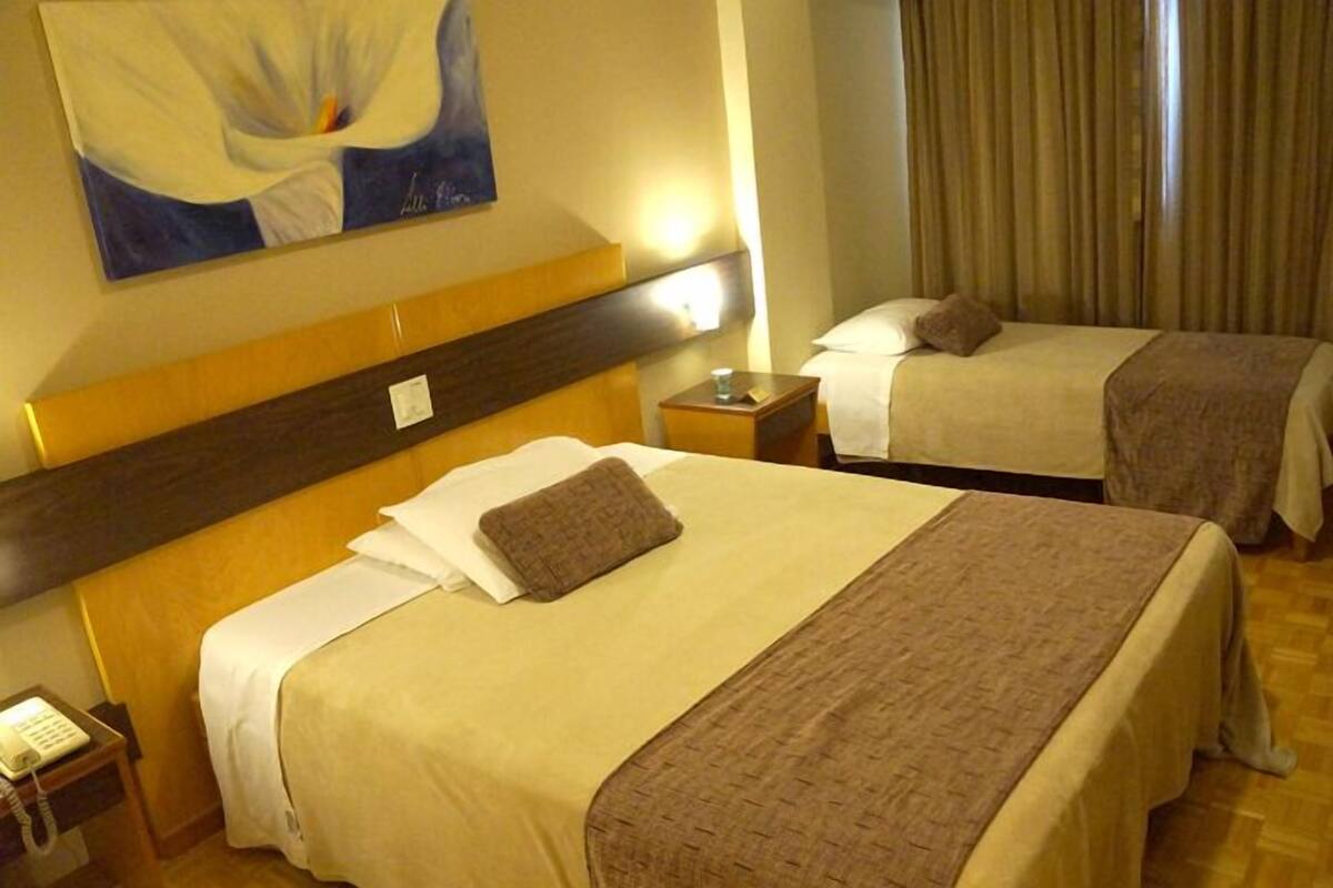 A hotel room with two beds, a wooden headboard, a painting on the wall, and a nightstand with a lamp.