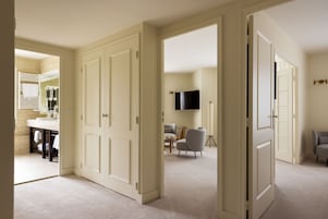 A spacious living area with a large white door, a flat-screen TV mounted on the wall, and a seating area with two chairs.