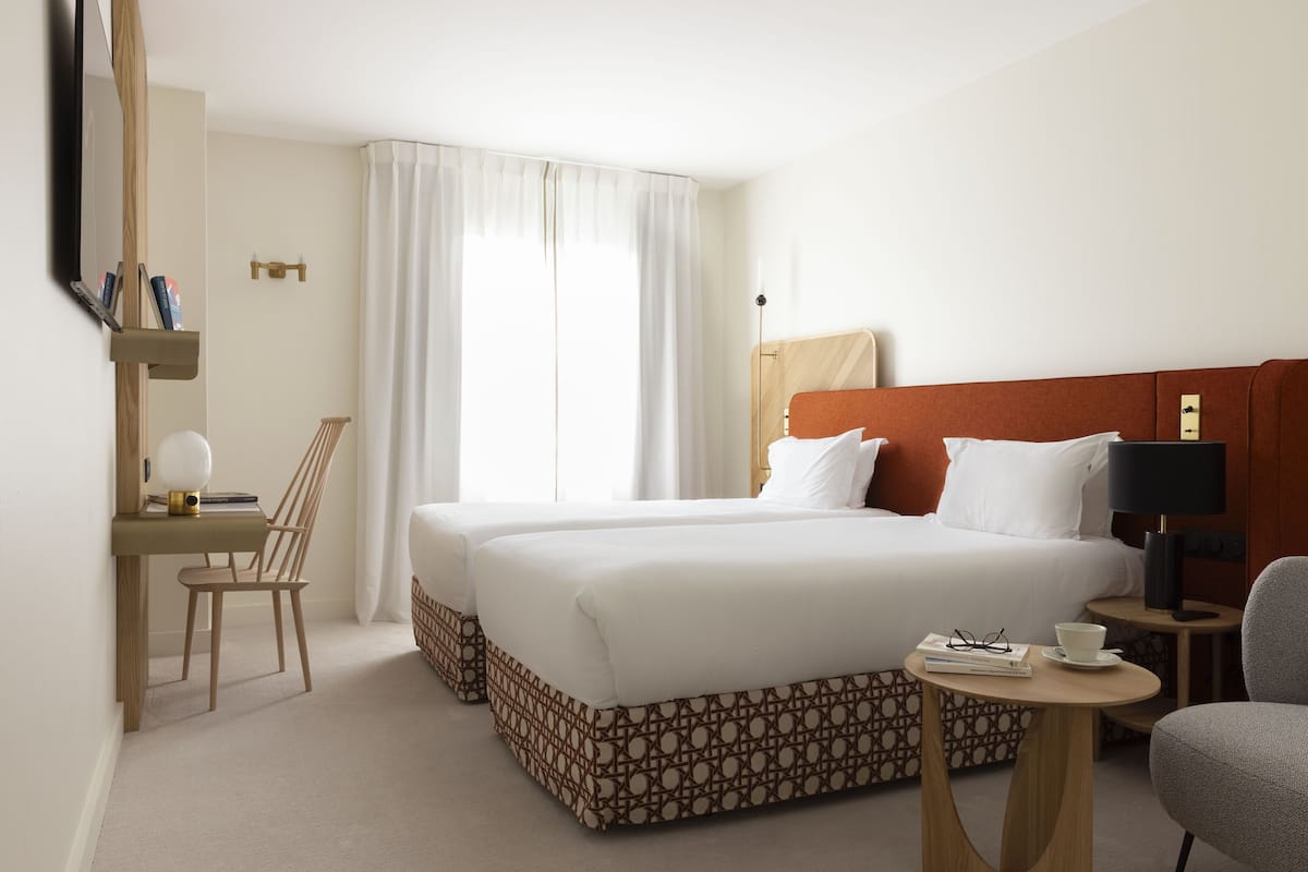 A hotel room with a large bed, a desk with a chair, a small table, and a lamp.