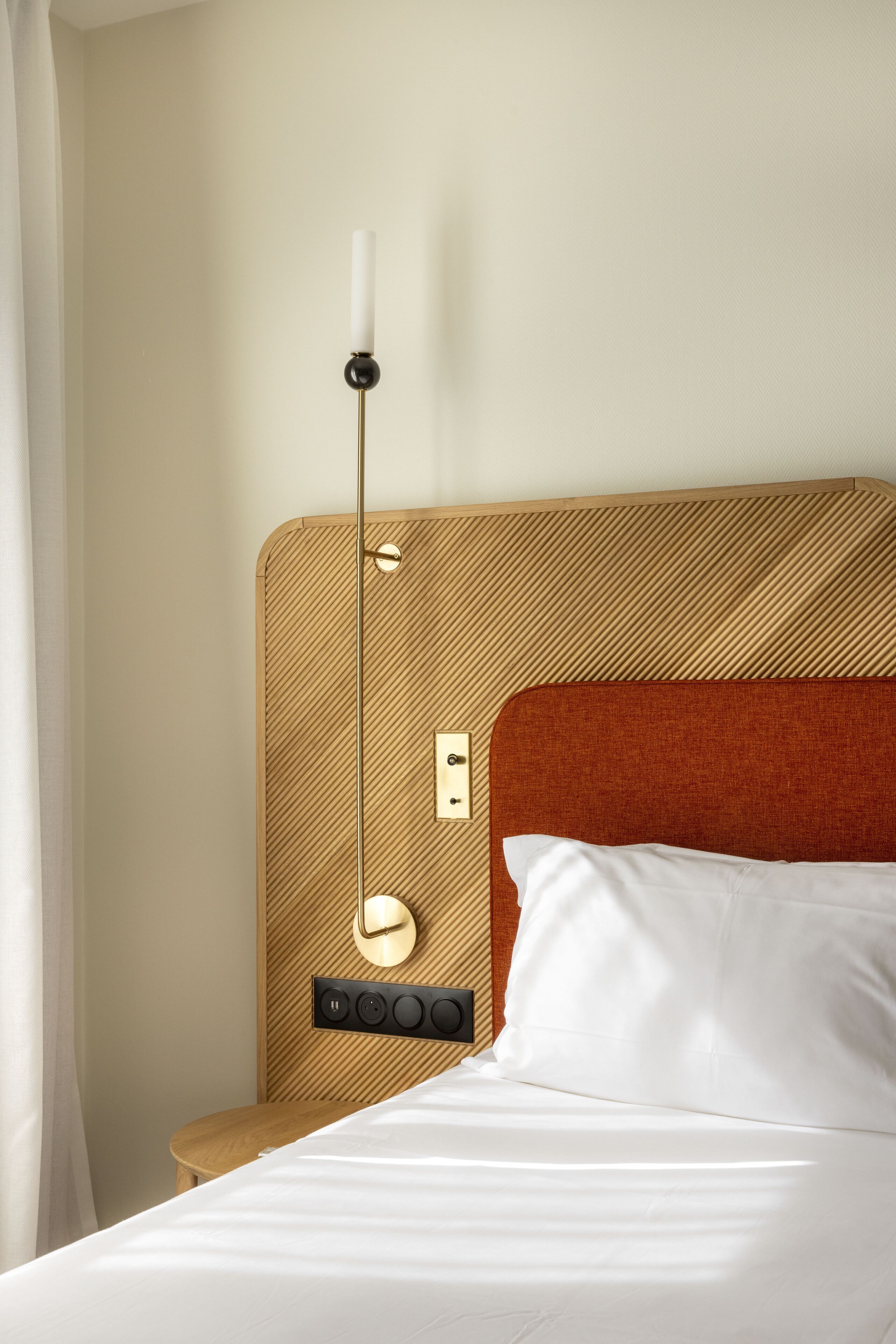 Una habitación de hotel con cama, mesita de noche, lámpara de pared y toma de corriente.