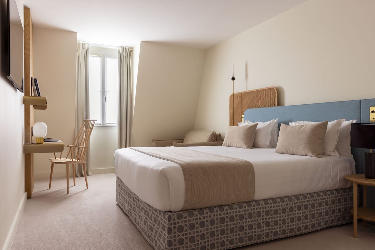 A bedroom with a large bed, a desk, a chair, and a window with curtains.