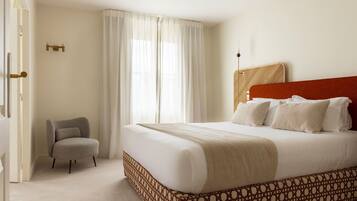 A hotel room with a large bed, a chair, and a window with curtains.