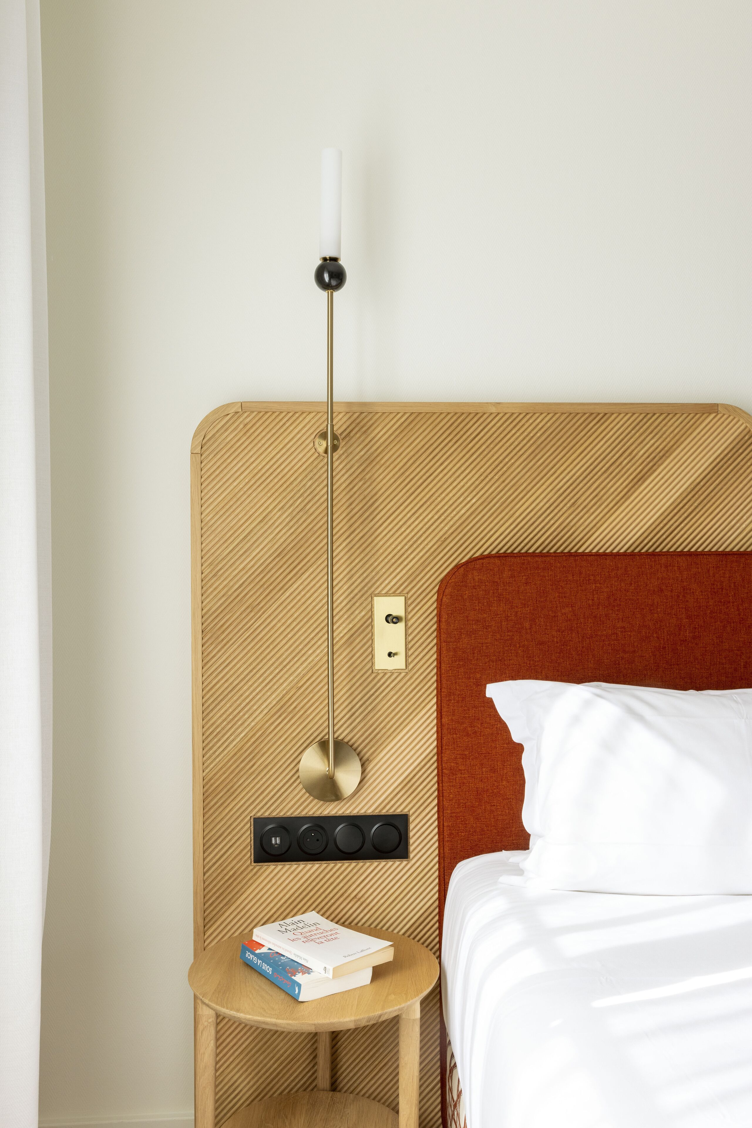 A hotel room with a wooden headboard, a bedside table with a lamp, and a bed with white bedding.