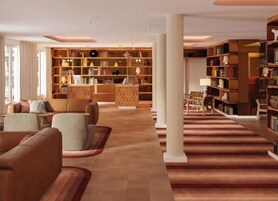 A spacious library with multiple bookshelves, comfortable seating, and a warm wooden floor.