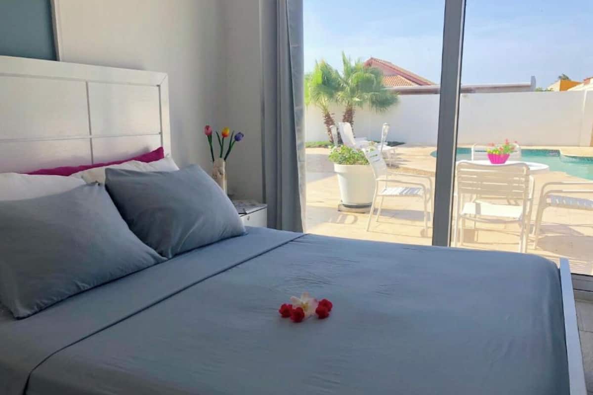 A bedroom with a large bed, a view of a pool and outdoor seating, and a white headboard.
