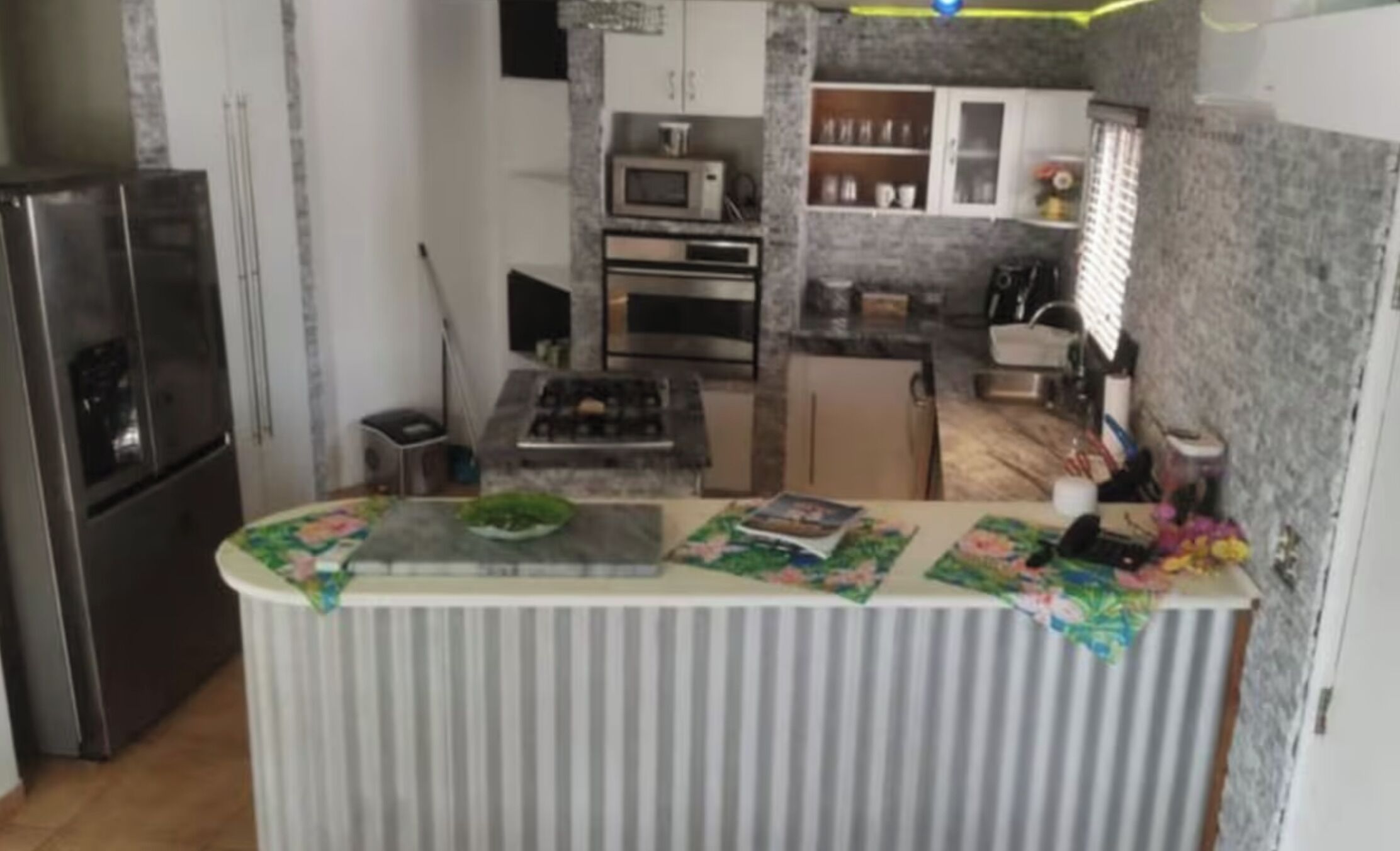 Una cocina con una isla central, refrigerador, microondas, horno y pileta.