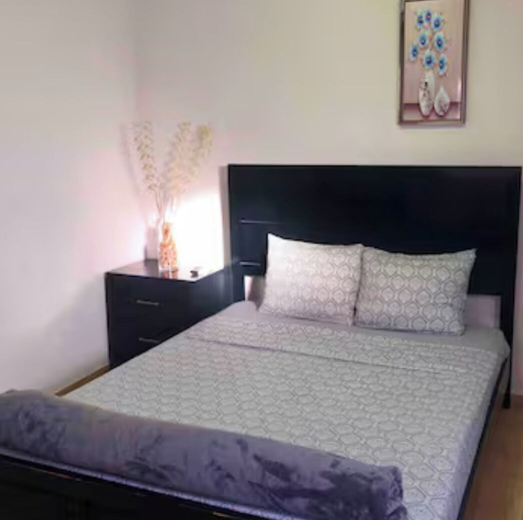 Une chambre à coucher comprenant un lit, une table de chevet, une lampe et une œuvre d’art accrochée au mur.