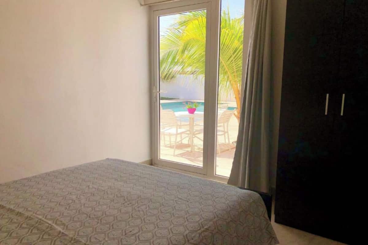 A bedroom with a bed, a window, and a view of an outdoor pool area.