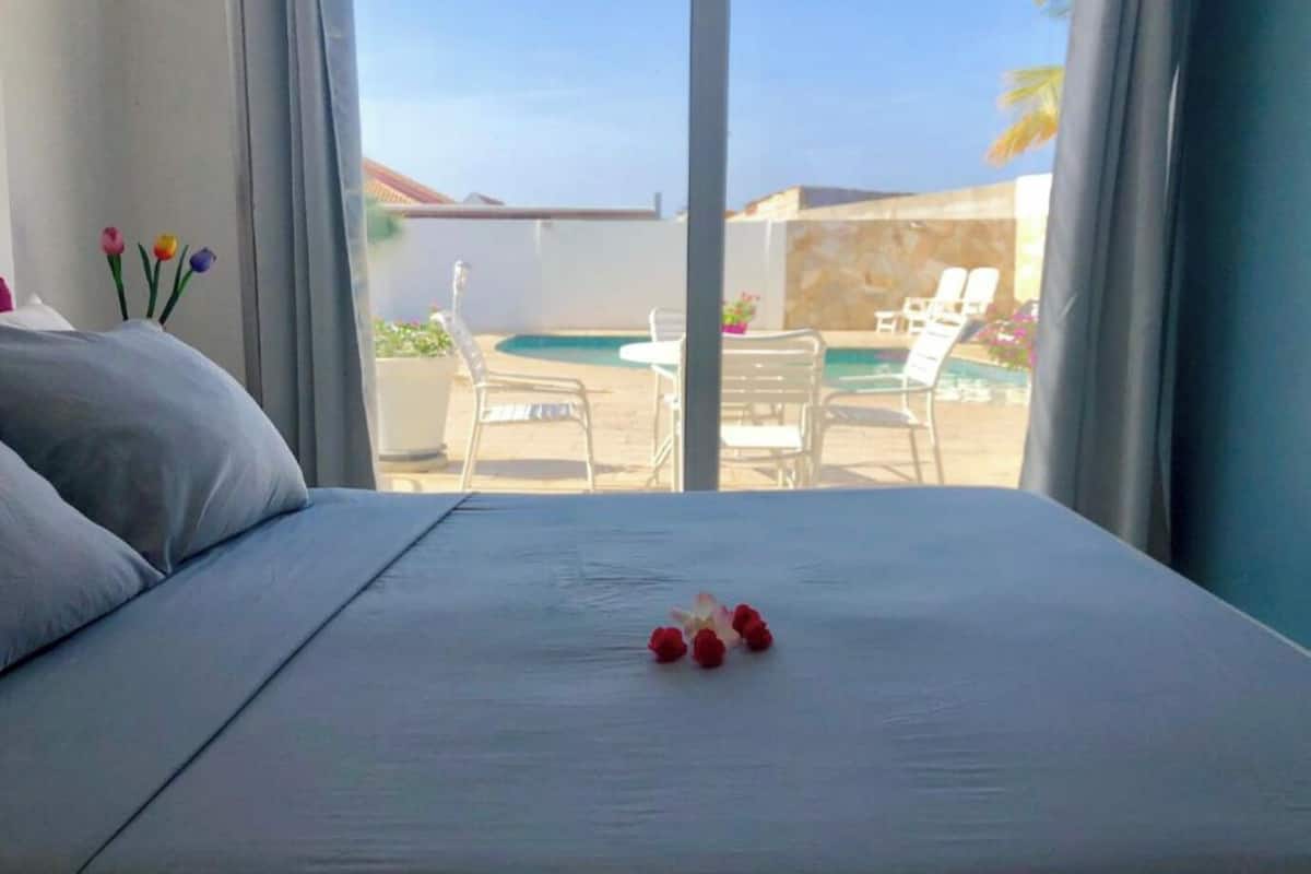A hotel room with a bed, a view of a pool area, and outdoor seating.