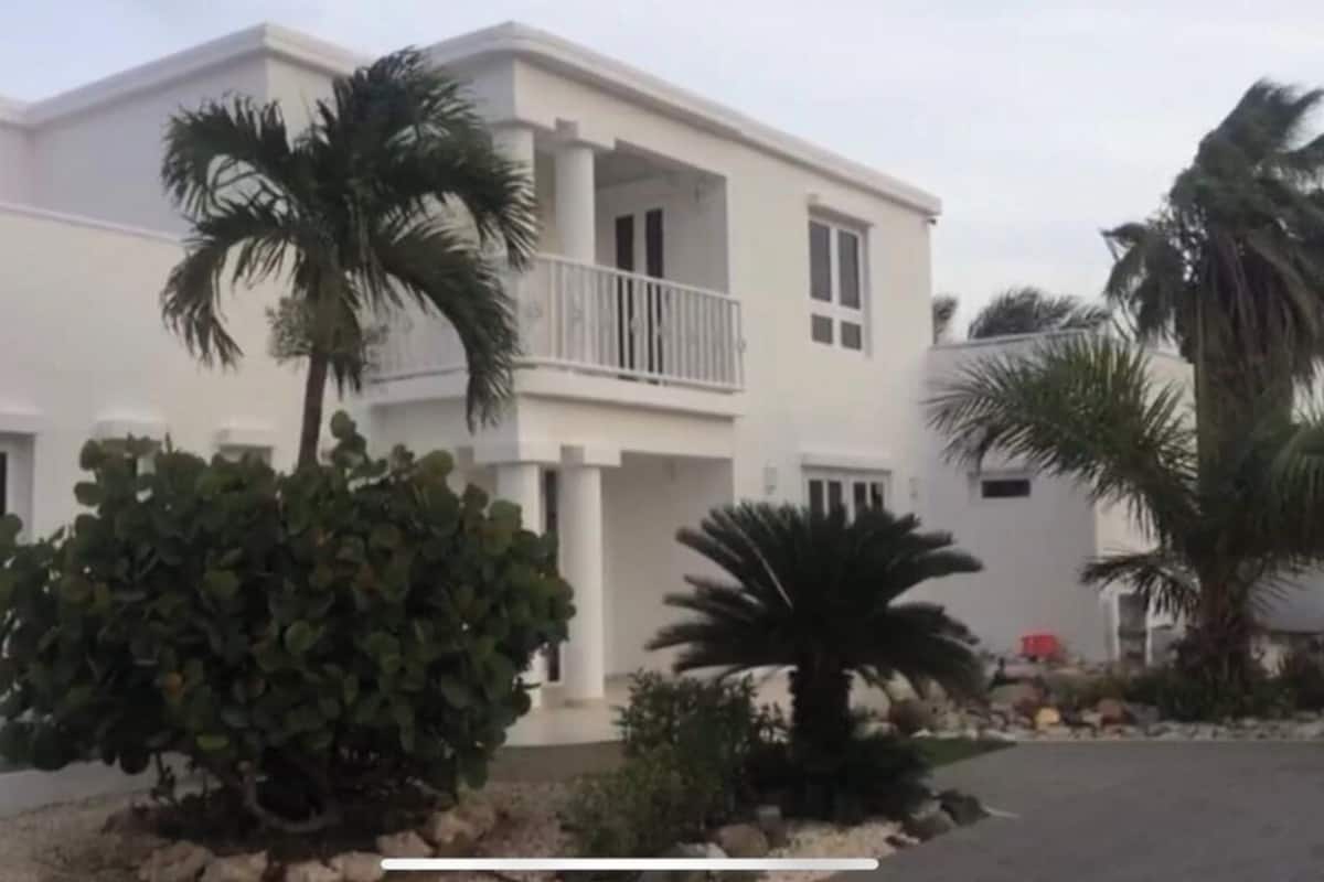 A two-story building with a balcony, surrounded by palm trees and shrubs.