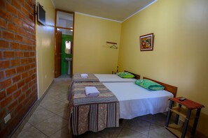 A hotel room with two beds, a small table, a TV, and a bathroom visible through an open door.