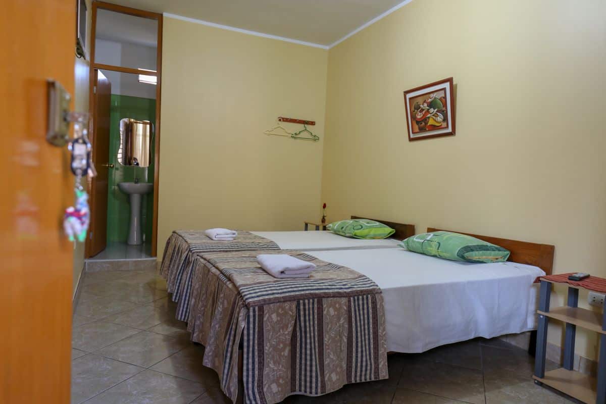 A hotel room with two beds, a sink, and a painting on the wall.