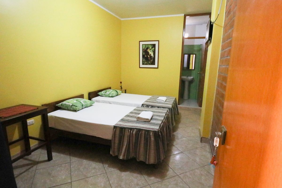 Una habitación con dos camas, una mesita y una puerta que da a otra estancia.