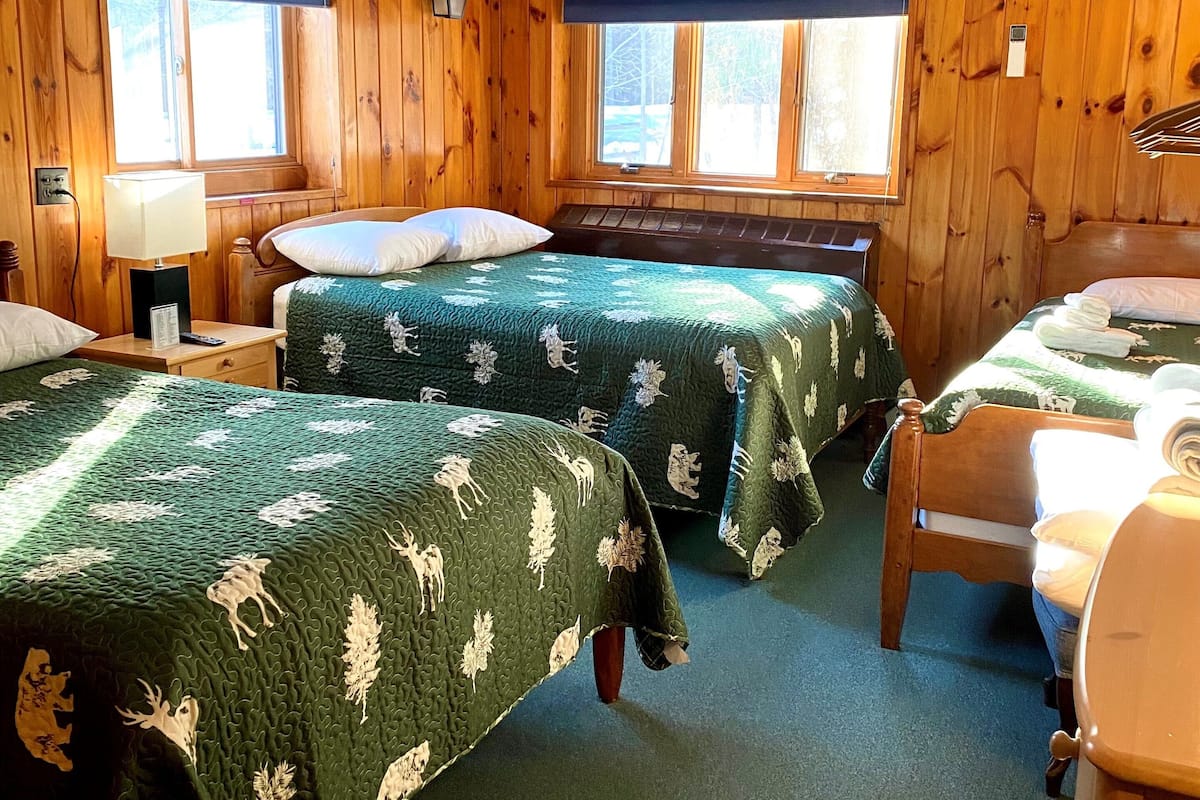 Una habitación tipo cabaña con dos camas, paredes de madera y ventanas amplias.