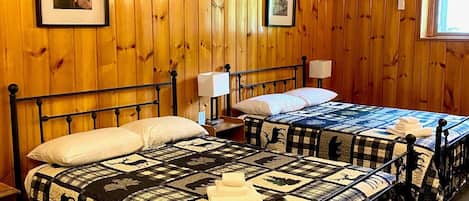 A room with two beds, wooden walls, framed pictures, and a window.