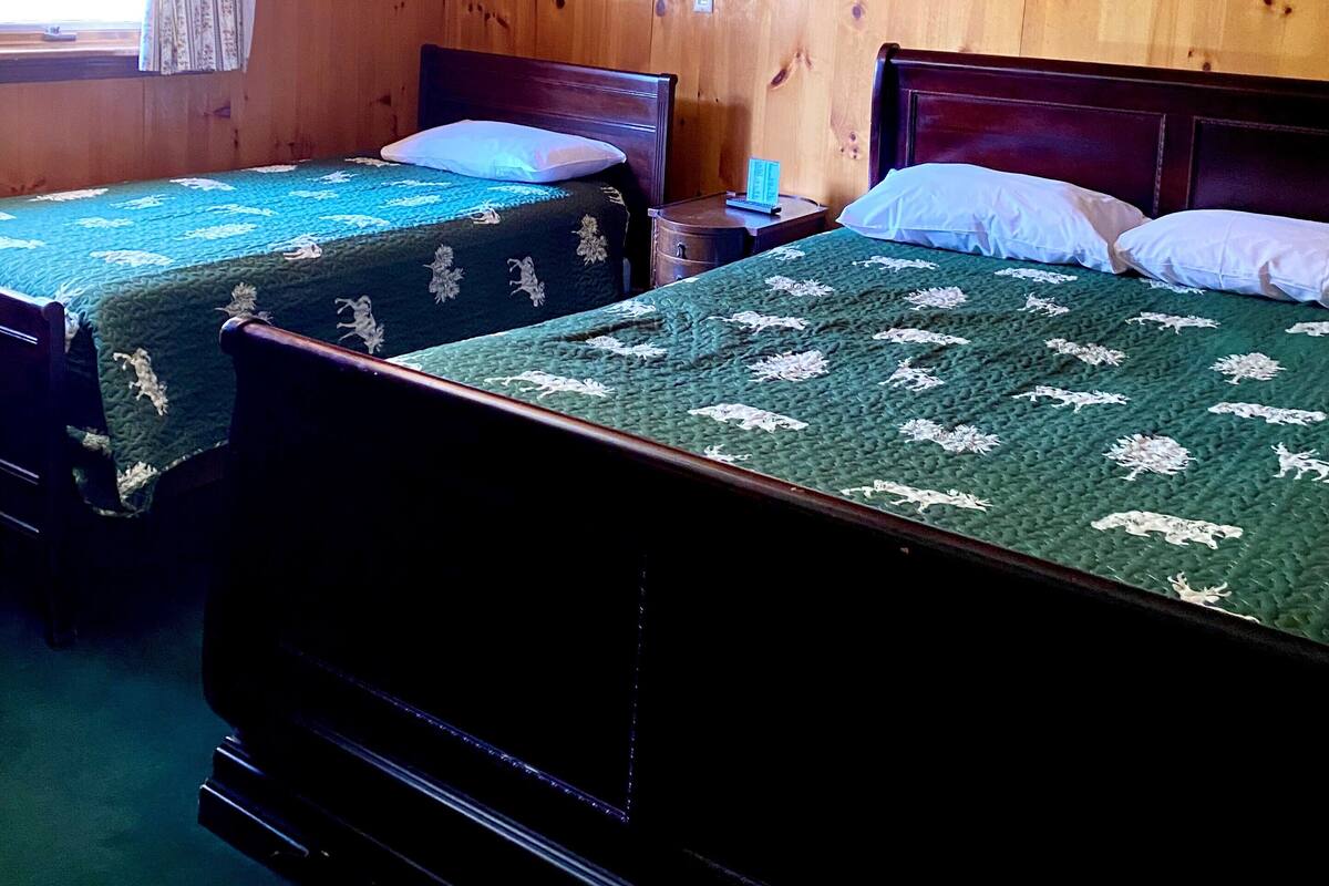 Una habitación con dos camas de madera, techo de madera y dos lámparas fijadas a la pared.