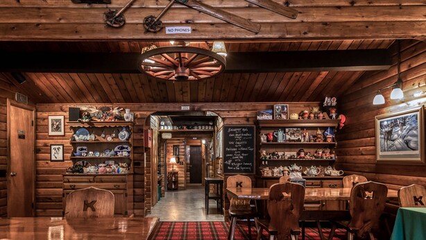 Un restaurante acogedor de estilo cabaña, con paredes de madera, alfombra escocesa y una variedad de platos exhibidos en estantes.