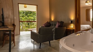Un baño moderno con una bañera grande, una silla de madera, un sofá y un balcón con vistas a zonas verdes.