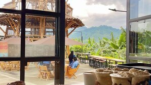 Un café con amplios ventanales que ofrecen vistas a una estructura de madera y vegetación exuberante.