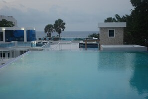 Una piscina en la azotea con vistas al mar, rodeada de edificios modernos y palmeras.