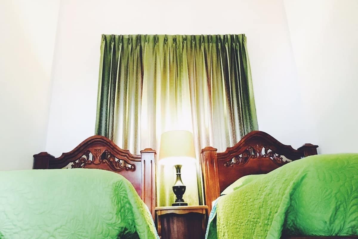Une chambre d’hôtel avec deux lits, une table de chevet avec une lampe et une fenêtre avec des rideaux.