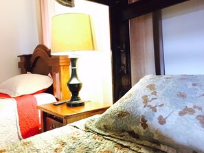 Ein Hotelzimmer mit einem Bett, einem Nachttisch mit Lampe, einem Fenster mit Vorhängen und einer Tür.