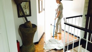Une personne est en train de laver un plancher en bois dans un couloir, avec un extincteur à proximité et des tableaux encadrés accrochés au mur.