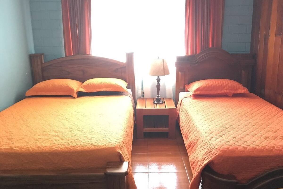 Une chambre avec deux lits, une table de chevet avec une lampe et une fenêtre avec des rideaux.