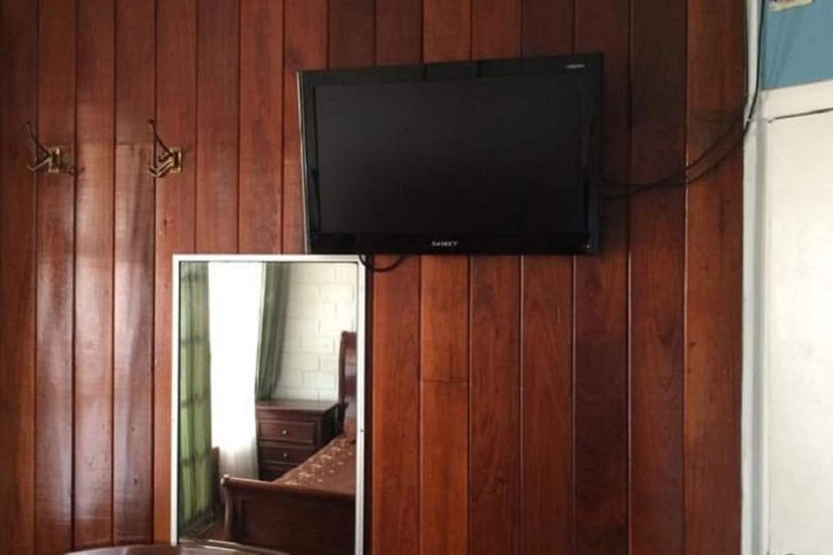 Une pièce aux murs lambrés, dotée d’un téléviseur à écran plat fixé au mur, et d’un miroir qui reflète un lit et une commode.