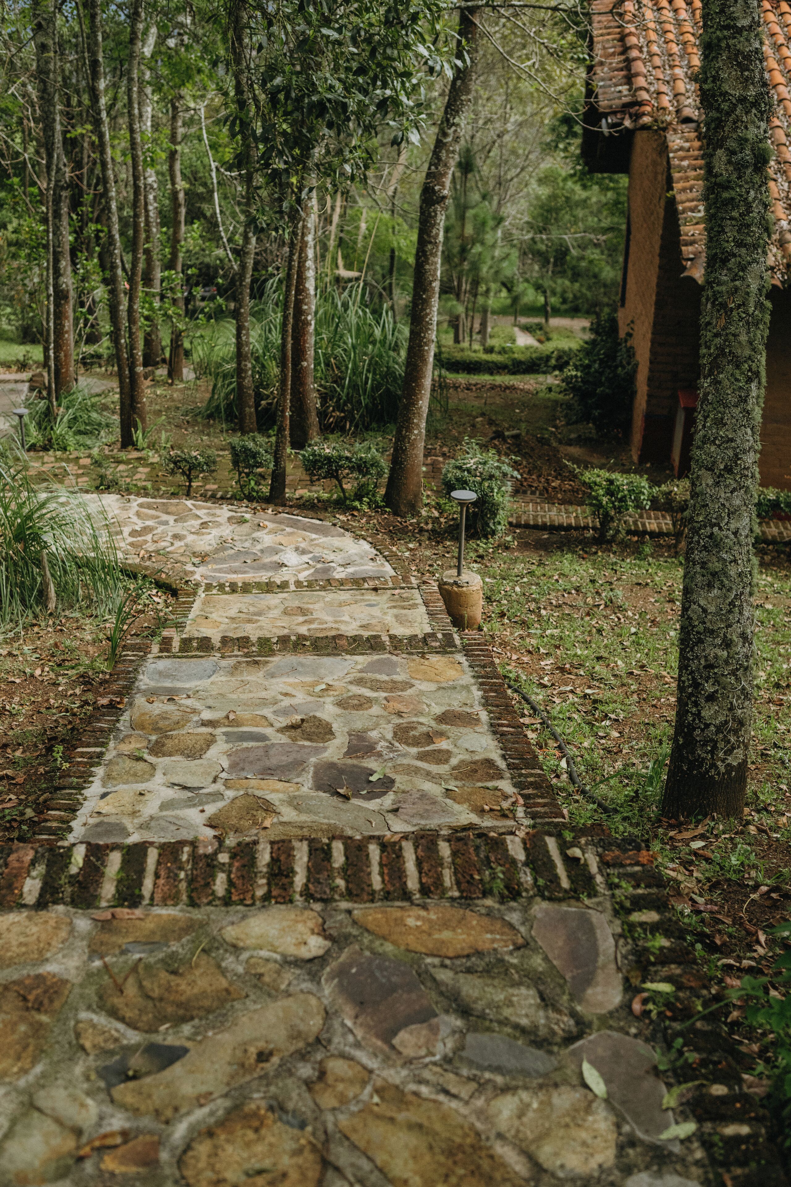 Un sendero de piedra que atraviesa un jardín con árboles y un pequeño edificio de ladrillo.