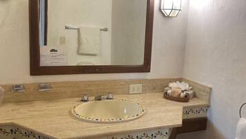 A bathroom with a large mirror, a sink with a decorative border, a towel rack, and a wall-mounted light fixture.