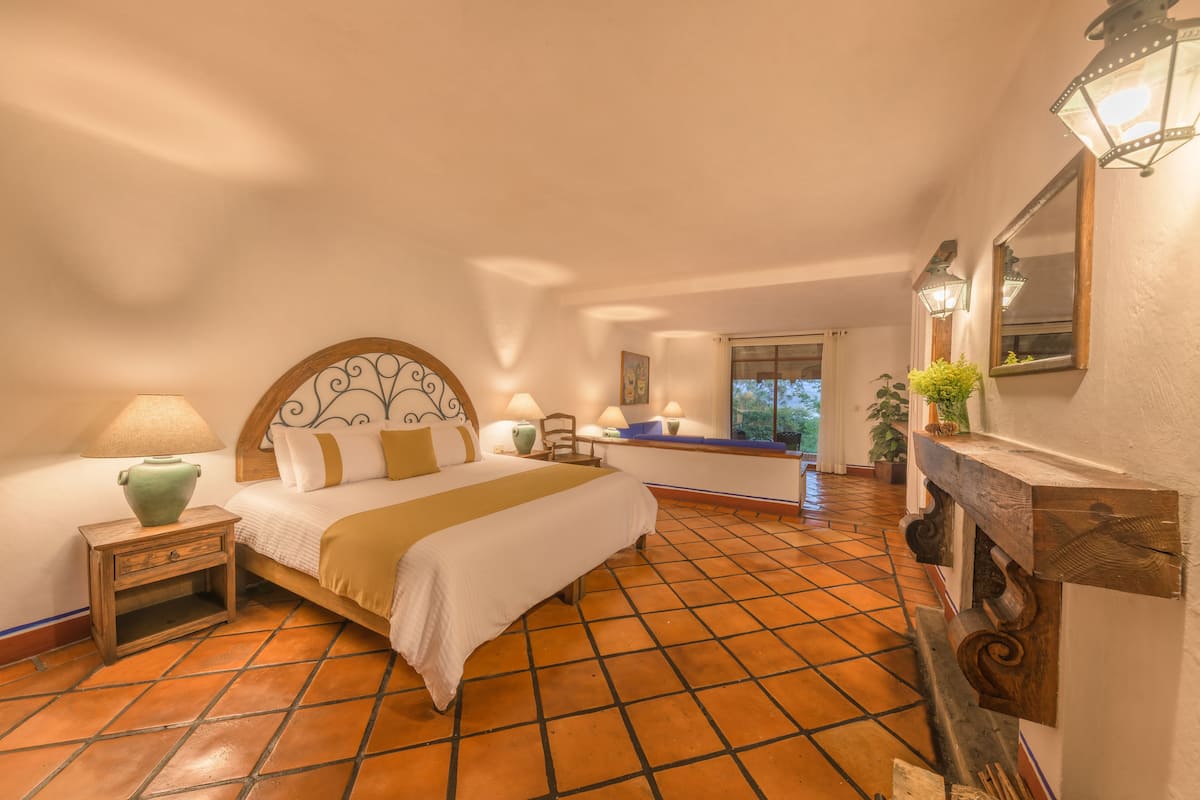Une chambre à coucher avec un grand lit, une table de chevet, une lampe, un miroir et une vue sur l’extérieur.