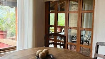 A round wooden table with a plate of three round objects, a wooden chair, and a view of an outdoor area with chairs and potted plants.