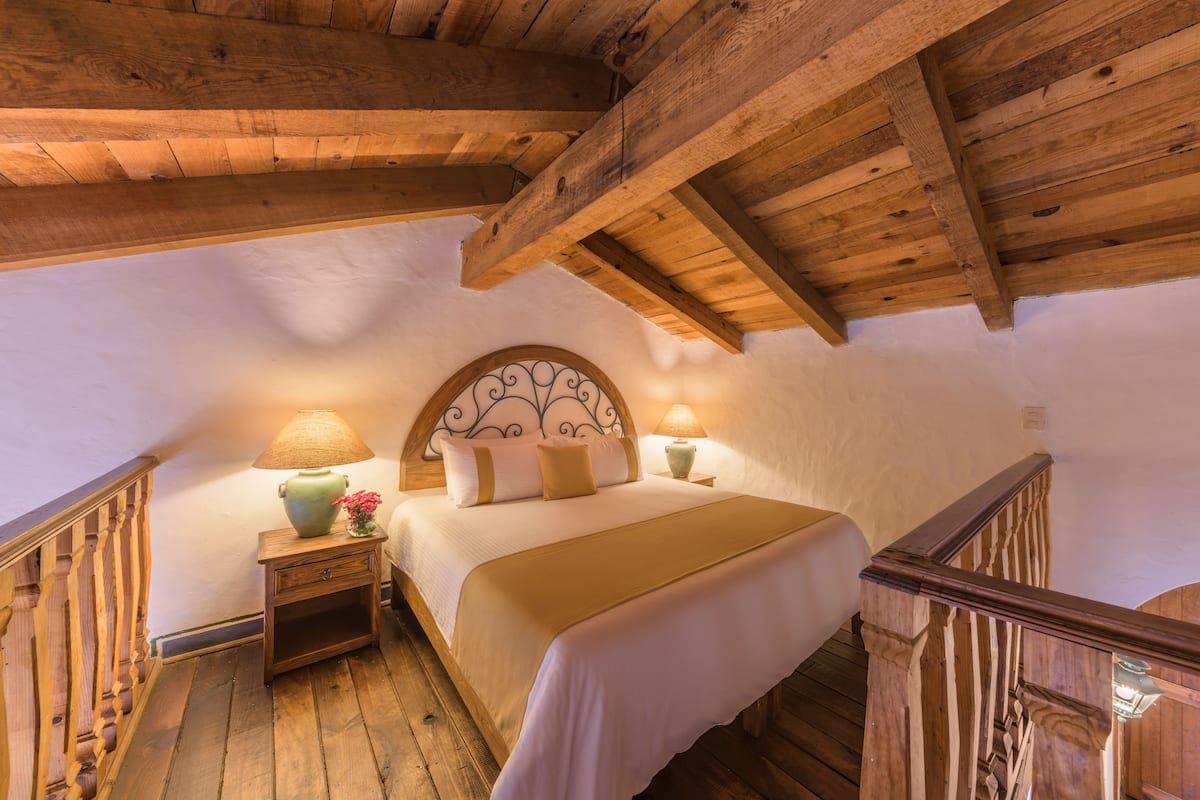 Une chambre avec un plafond en bois, un lit avec une literie blanche, deux lampes de chevet et une table de chevet ornée d’un vase.
