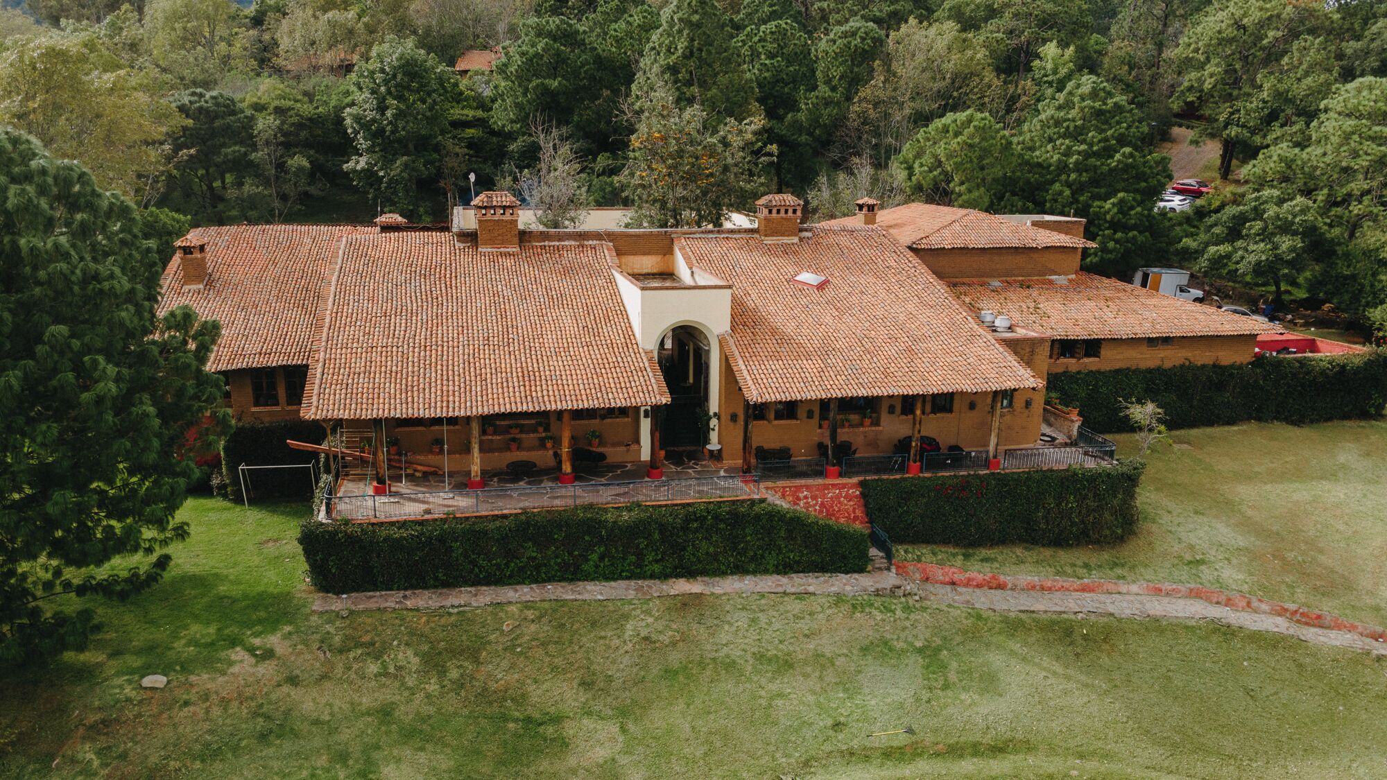 Un grand bâtiment à plusieurs étages, doté d’un toit en tuiles, entouré de haies bien entretenues et d’une pelouse.