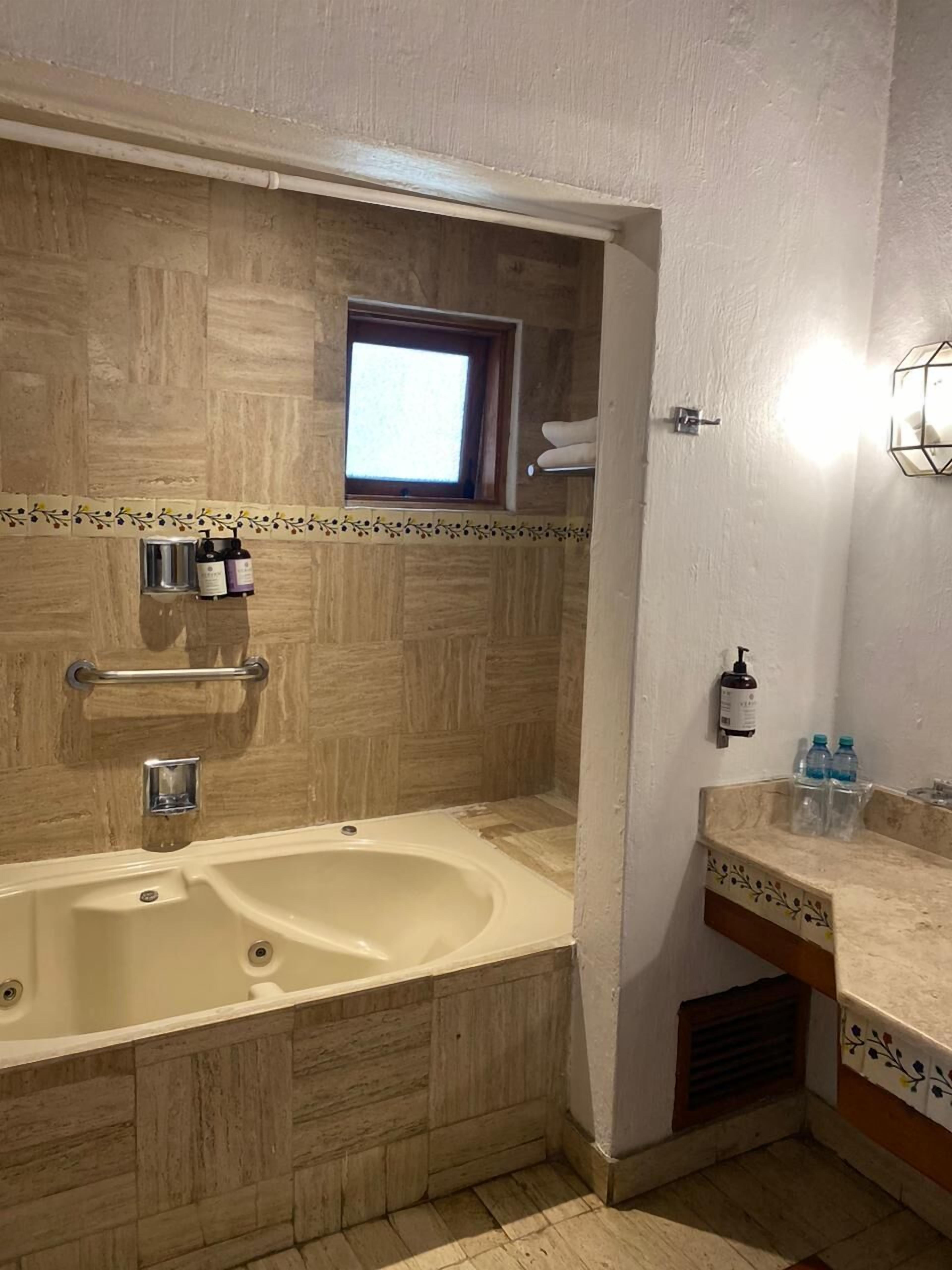 A bathroom with a large bathtub, a window above the sink, and a towel rack.