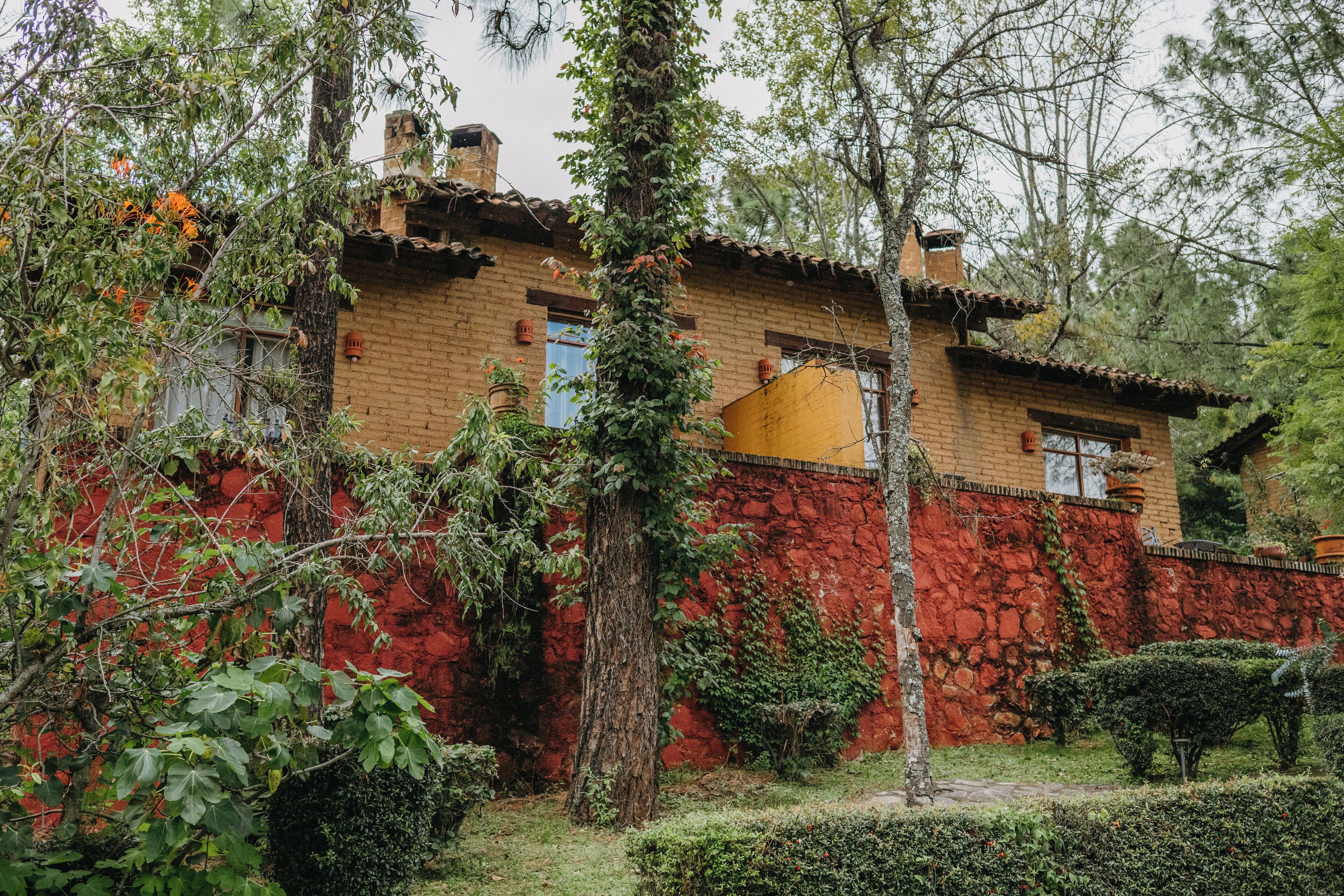 Um edifício rústico com fachada de tijolos, parede de pedra vermelha e um jardim com diversas plantas e árvores.