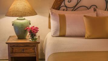 A neatly made bed with a headboard, a bedside table with a lamp, and a vase with flowers.