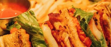 Un sándwich con lechuga, tomate y queso, acompañado de papas fritas y un pequeño recipiente de kétchup.