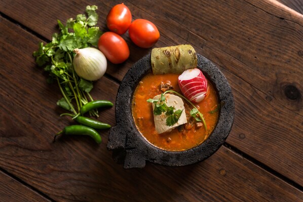 Un tazón de sopa con verduras y hierbas sobre una mesa de madera.