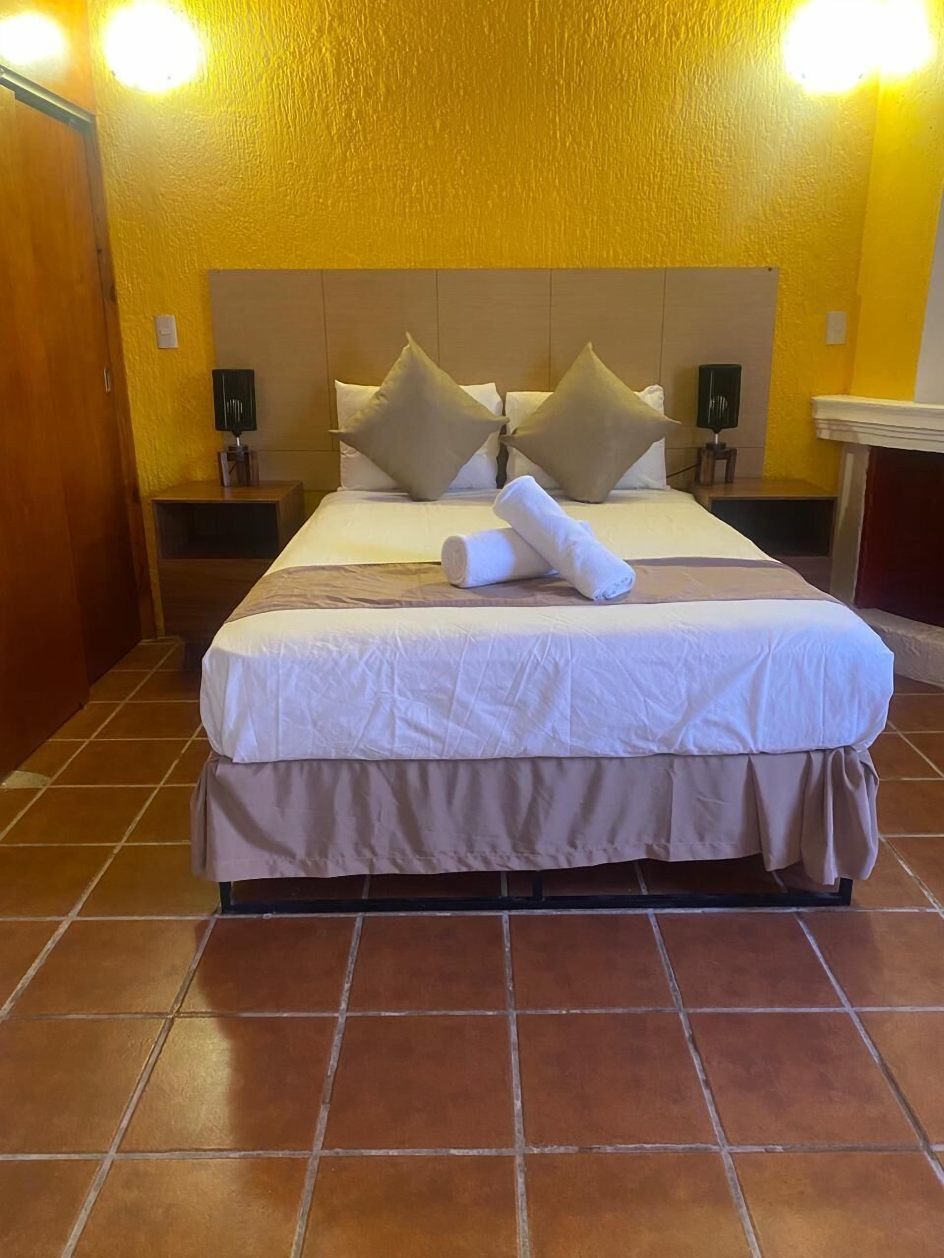 A hotel room with a large bed, two nightstands, a wooden door, and a tiled floor.