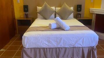 A hotel room with a large bed, two nightstands, a wooden door, and a tiled floor.
